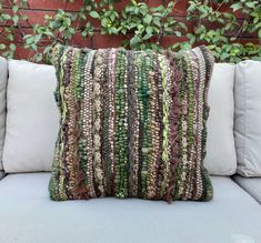 a green and brown pillow sitting on top of a white couch next to a brick wall