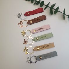 six keychains with names on them sitting next to a plant