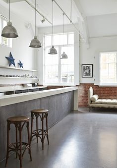 an open kitchen with two stools in front of the bar and windows above it