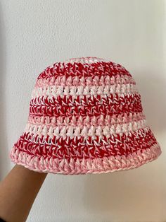 a crocheted red and white hat is held up by a person's hand