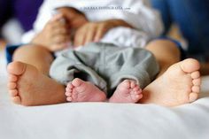 a baby laying on top of a bed next to his mother's legs and feet