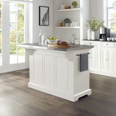 a white kitchen with an island in the middle and open shelves on both sides, along with lots of natural wood flooring