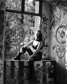 a woman sitting on top of a window sill next to a wall covered in graffiti