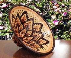 a wooden bowl sitting on top of a table next to some bushes and pink flowers