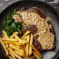 steak with gravy and french fries in a black plate on a wooden table