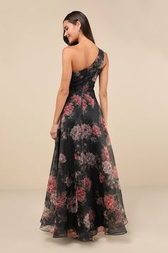 a woman wearing a black floral print dress with one shoulder and open back, looking down at the floor