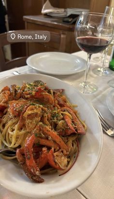 a white plate topped with pasta covered in shrimp and sauce next to a glass of wine