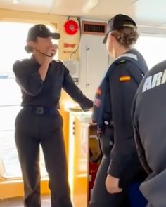 two women in uniform are shaking hands on a boat while another woman is standing next to them