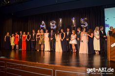 a group of people standing on a stage in front of a number five sign with balloons