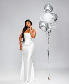 a woman in a white dress standing next to a bunch of silver and white balloons