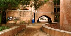 an arched walkway between two brick buildings with trees on either side and another building in the background