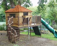 a wooden play structure with a green slide in the foreground and trees in the background