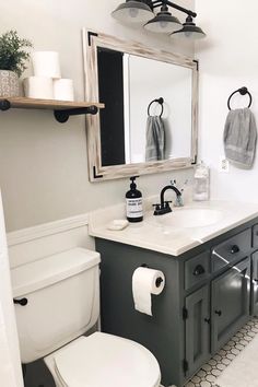 a white toilet sitting under a bathroom mirror next to a sink and a toilet paper dispenser