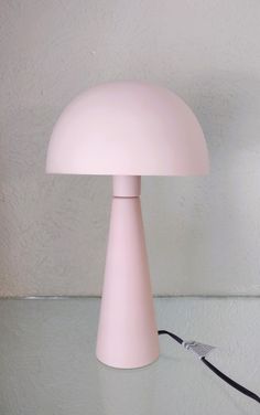 a pink lamp sitting on top of a table next to a black cord and a white wall