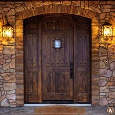 a wooden door with two lights on each side and a brick wall behind it, in front of a stone building