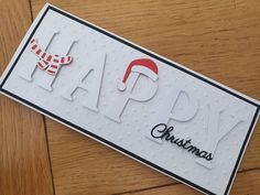 a card with the words happy christmas written in black and white, on a wooden surface