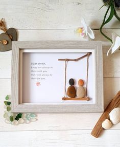 two pebbles sitting on a swing in a shadow frame with flowers and rocks