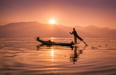 a man standing on top of a boat in the middle of water with mountains in the background