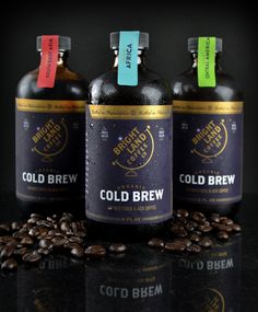 three bottles of cold brew sitting next to coffee beans on a black surface with colored labels