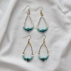 three pairs of beaded earrings on top of a white cloth covered sheet with gold and turquoise beads