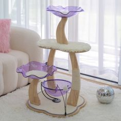 a cat tree in the corner of a living room with white carpet and pink pillows