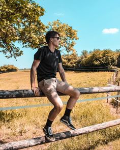 a man sitting on top of a wooden fence in front of a field with trees