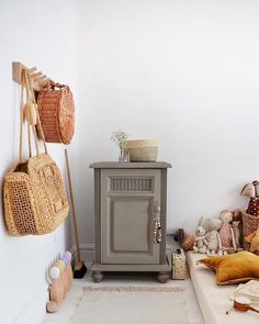 a small cabinet with baskets hanging on it's sides next to a bed and stuffed animals