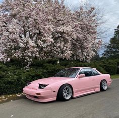 a pink car is parked on the side of the road in front of some trees