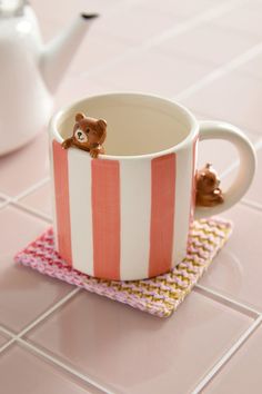 a tea cup with a teddy bear in it sitting on a pink and white tile floor