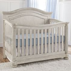 a white baby crib in a room with blue and white curtains on the windowsill