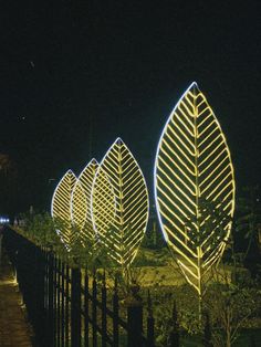 three large leaf shaped lights are lit up in the night sky behind a black fence