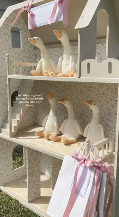 there are many stuffed ducks on the shelves in this doll house display case with pink ribbon