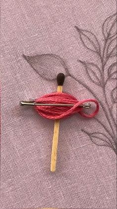 a pair of knitting needles are hooked up to a piece of red yarn on a pink cloth