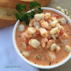 a bowl of soup with shrimp and bread on the side