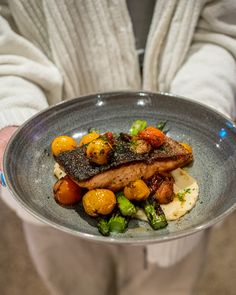 a person holding a plate with meat and vegetables on it in front of their hands