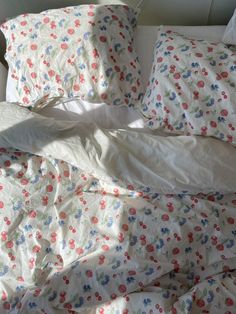 an unmade bed with white sheets and colorful flowers