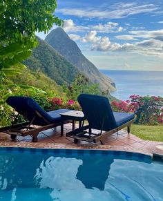 two lounge chairs sitting next to a swimming pool with the ocean and mountains in the background