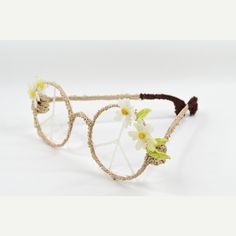 a pair of glasses with flowers on the rim and wire around it, sitting on a white surface