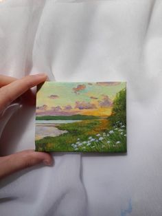 a person holding up a small piece of paper with a painting on it's side