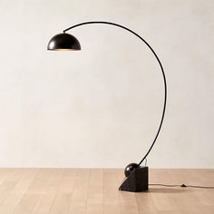 a floor lamp with a black shade on the base and a white wall in the background