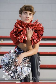 a young man sitting on top of a bench holding a cheerleader pom pom