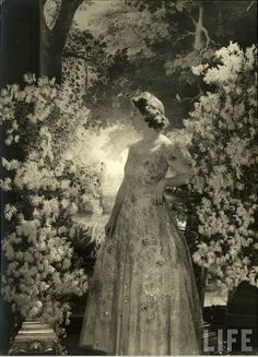 an old black and white photo of a woman in a dress with flowers on it