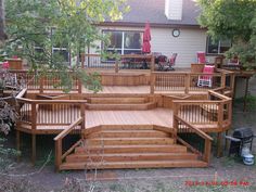 a wooden deck with steps and railings in front of a house surrounded by trees