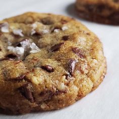 two chocolate chip cookies sitting on top of a white tablecloth next to each other