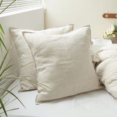 a bed topped with white pillows next to a plant