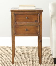 a small wooden table with two drawers on top and a white chair in the background