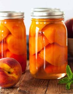 two jars filled with peaches sitting on top of a wooden table next to an apple