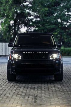 the front end of a black range rover parked on a cobblestone road with trees in the background