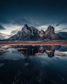 the mountain range is reflected in the still water at sunset, with dark clouds overhead