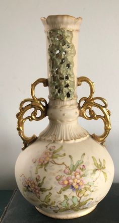 a white vase with flowers painted on the side and gold trimming around the top